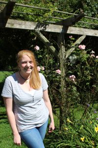 Ellie stands in a garden smiling at the camera.